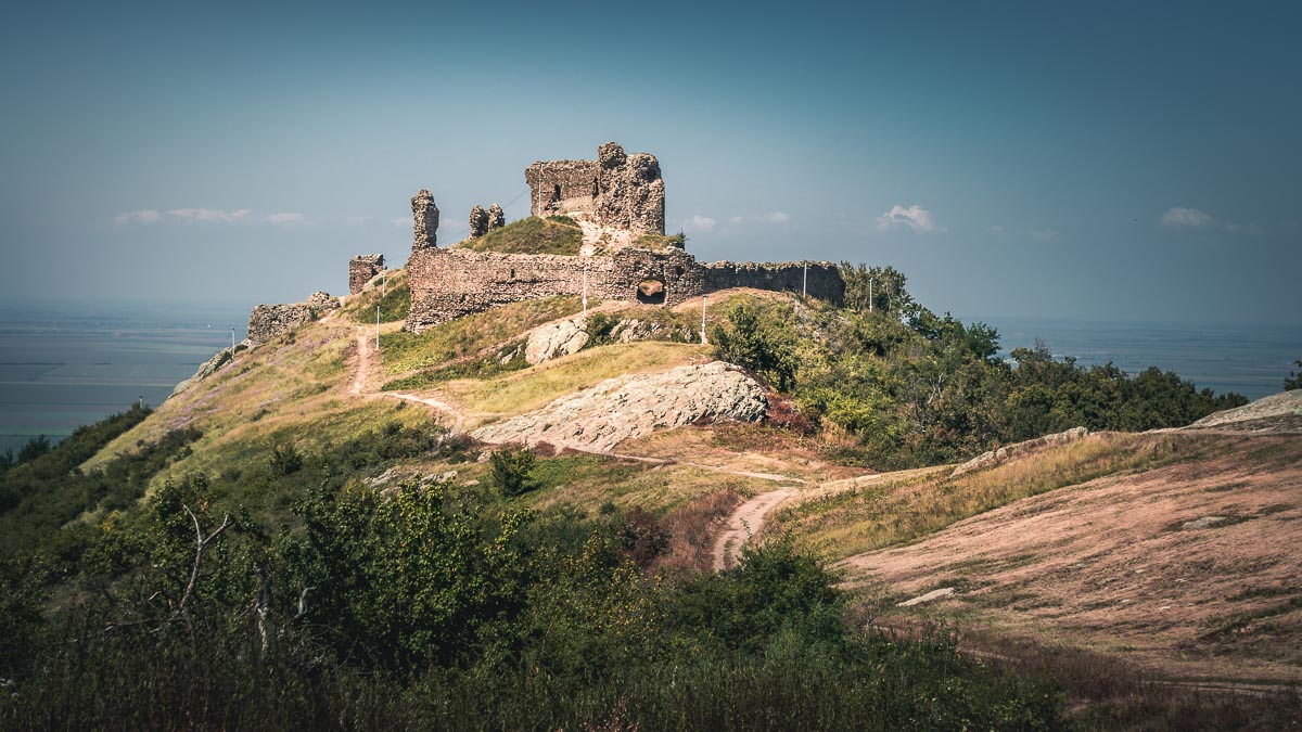 The Șiria fortress on the edge of the hill with a large plain in the background.